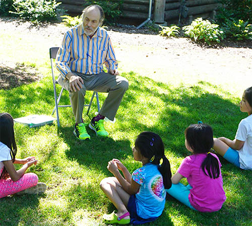 man seated beard outdoors telling stories children listening